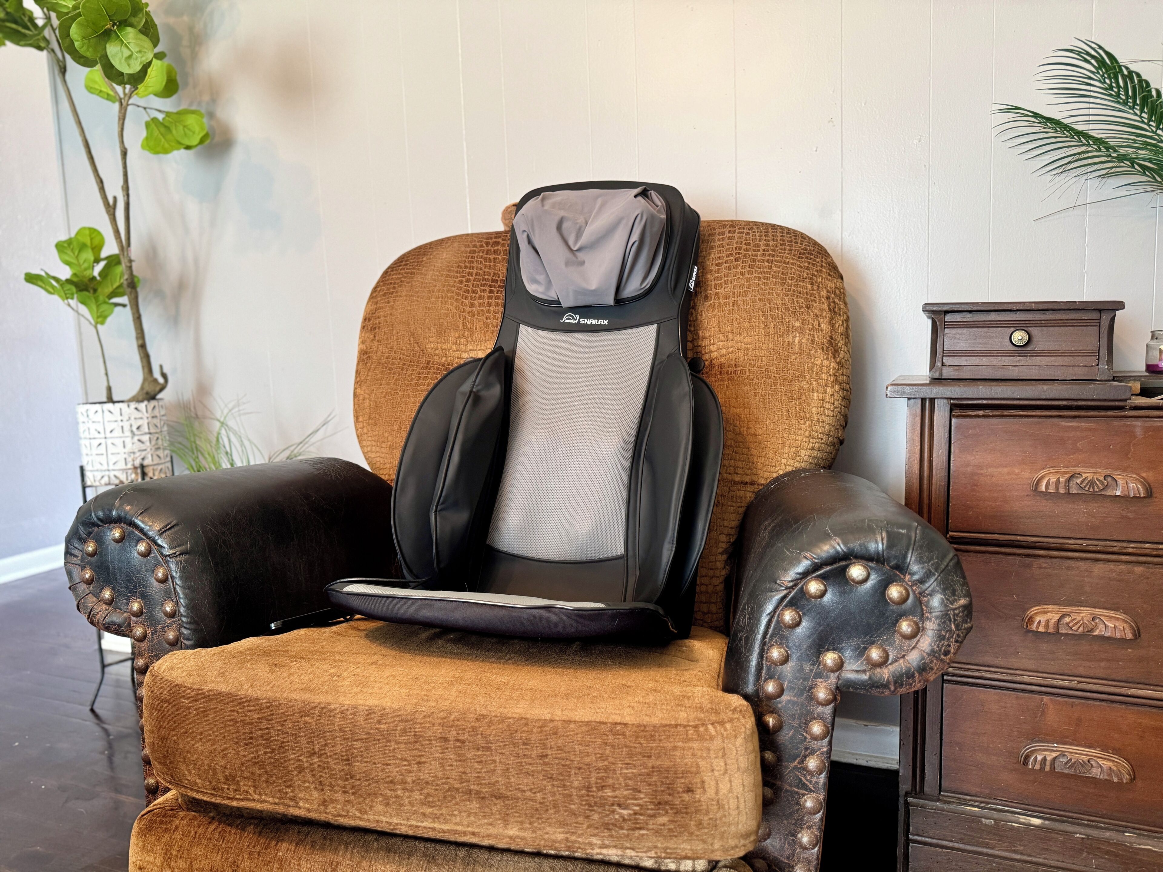 Un fauteuil de massage doté d’un repose-tête et d’un repose-pieds, placé à côté d’une commode en bois et d’une plante en pot.