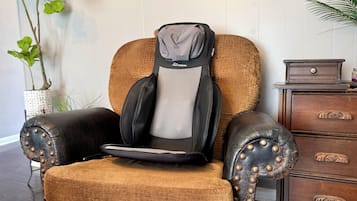 Un fauteuil de massage doté d’un repose-tête et d’un repose-pieds, placé à côté d’une commode en bois et d’une plante en pot.