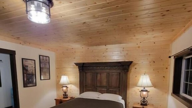 A wooden-paneled room with a bed, two bedside lamps, and a window. - Crescent Motel (Crescent)