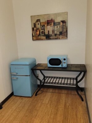 Ett litet pentry med ett blått kylskåp, en mikrovågsugn och ett svart metallbord.