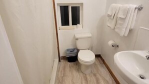 A bathroom with a toilet, a window, a sink, and a towel rack. - Crescent Motel (Crescent)