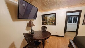 A dining area with a table and chairs, a mounted television, and a painting on the wall. - Crescent Motel (Crescent)
