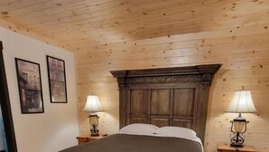 A wooden-paneled bedroom with a large bed, two bedside tables with lamps, and framed pictures on the wall. - Crescent Motel (Crescent)