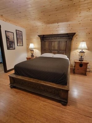 A wooden-paneled bedroom with a large bed, two bedside tables with lamps, and framed pictures on the wall. - Crescent Motel (Crescent)