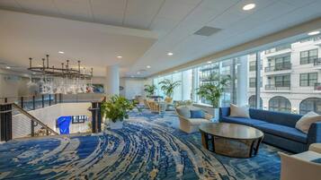 A spacious lobby with a blue patterned carpet, seating areas, large windows, and a staircase.