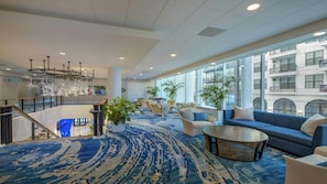 A spacious lobby with a blue patterned carpet, seating areas, large windows, and a staircase.