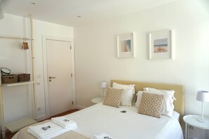 Habitación de hotel con cama, dos almohadas, mesita de noche, lámpara, cuadro en la pared, armario y toallero.