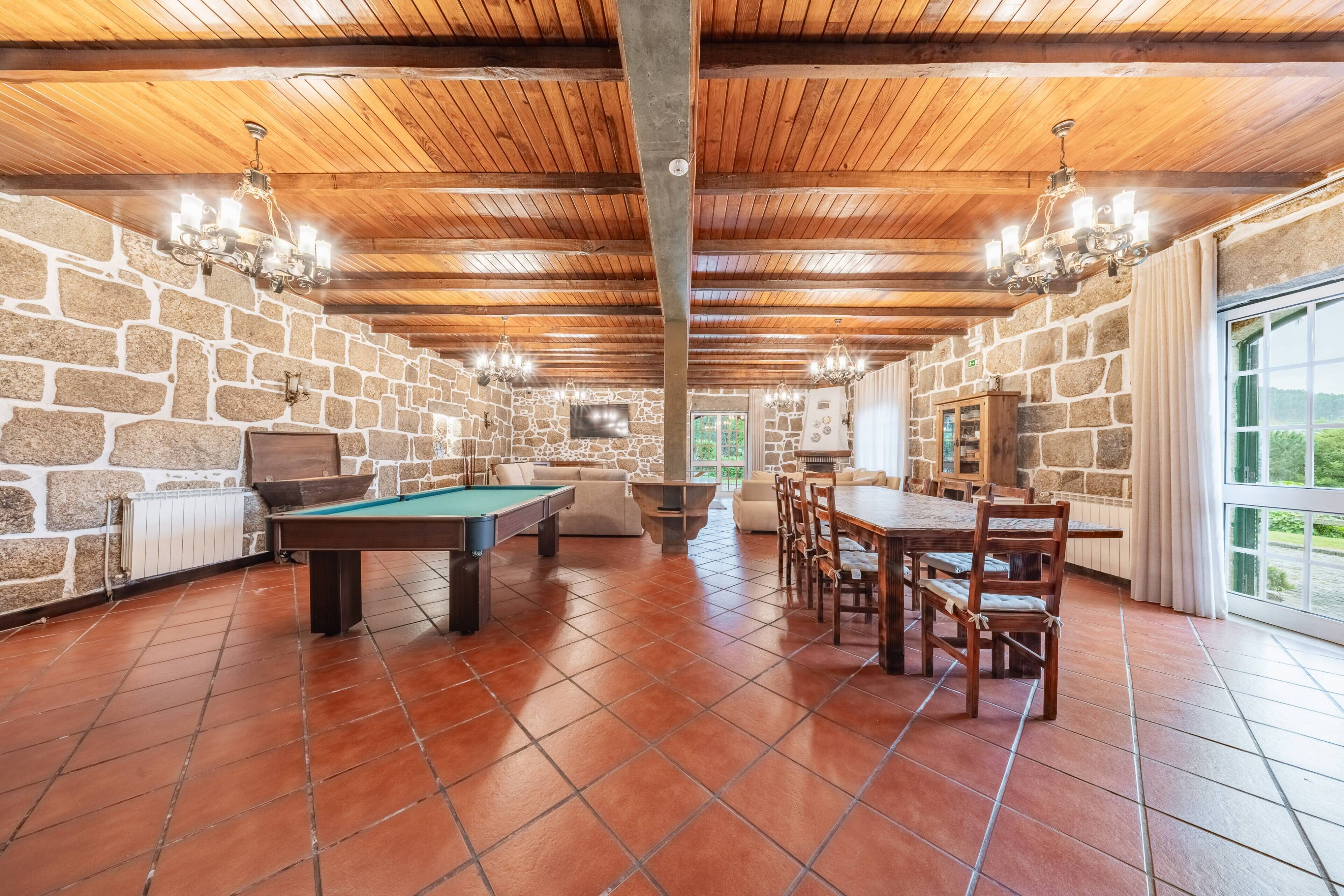 Una habitación con mesa de billar, una mesa de comedor con sillas, paredes de piedra y techo de madera.