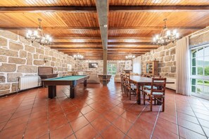 A room with a pool table, a dining table with chairs, stone walls, and a wooden ceiling.