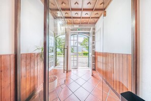 Un pasillo con paredes de madera, suelo de baldosas y una puerta de cristal que da al exterior.