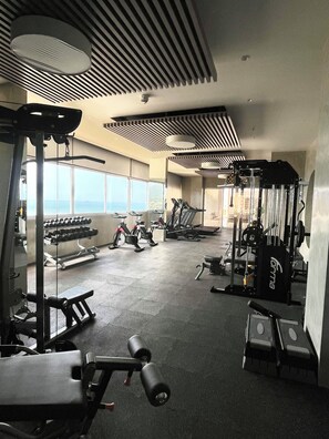Ein Fitnessstudio mit unterschiedlichen Trainingsgeräten, einer Bank und Kurzhanteln.