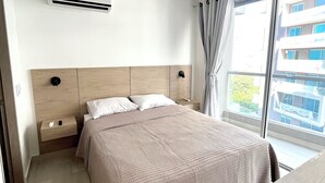 A hotel room with a bed, bedside tables, an air conditioning unit, a window with curtains, and a view of a building. - Marriott & Playa Dormida Area +Vista al Mar + Piscina infinity/jacuzzis (Magdalena)