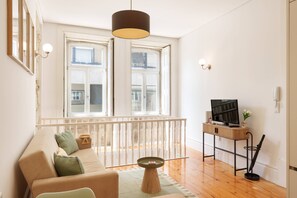 Ein Wohnzimmer mit einer Couch, einem kleinen Tisch, einem Fernseher auf einem Schrank und einem Balkon mit Geländer.