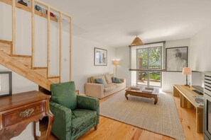 Een woonkamer met een trap, een groene fauteuil, een bank, een salontafel en een televisie.