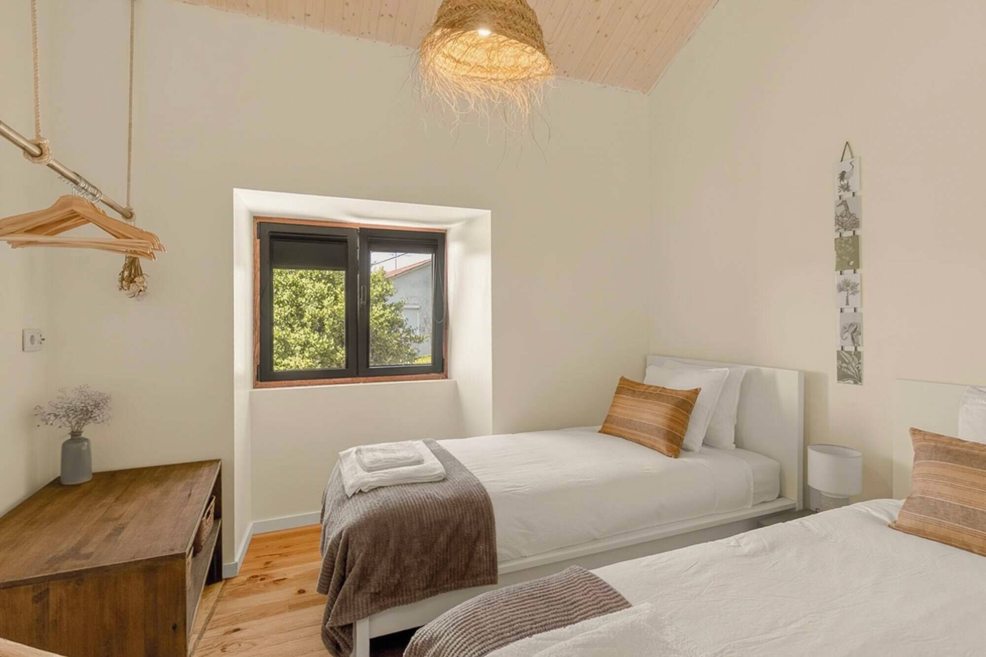 Une chambre avec deux lits, une fenêtre, une commode en bois et un luminaire suspendu.