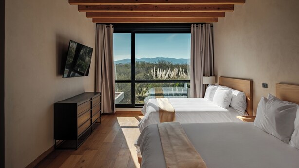 A bedroom with two beds, a TV on the wall, and a large window with a view of mountains. -  Casa Iremia by VIATO HOMES (San Miguel de Allende)