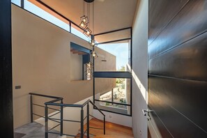 A modern staircase with a metal railing, a hanging light fixture, and a view of an outdoor garden through a large window.