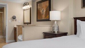 Una habitación de hotel con una cama, una mesita de noche con una lámpara, un espejo y un cuadro en la pared.