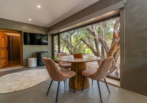 Un espace repas moderne avec une table ronde, quatre chaises et une grande fenêtre donnant sur la verdure.