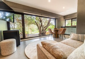 Un salon moderne doté d’une grande fenêtre, d’une table basse ronde, d’un canapé et d’un coin repas avec des chaises.