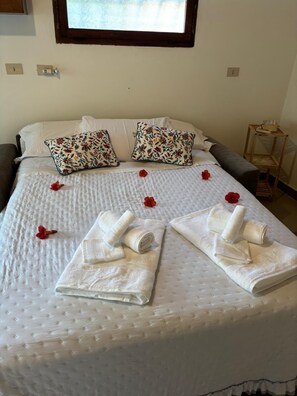 Ein ordentlich gemachtes Bett mit blumigen Kissen, gerollten Handtüchern und roten Blumen.