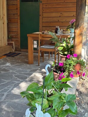 Ein Holztisch mit Stühlen vor einem Gebäude, das eine grüne Tür hat, umgeben von Blumentöpfen und Blumen.