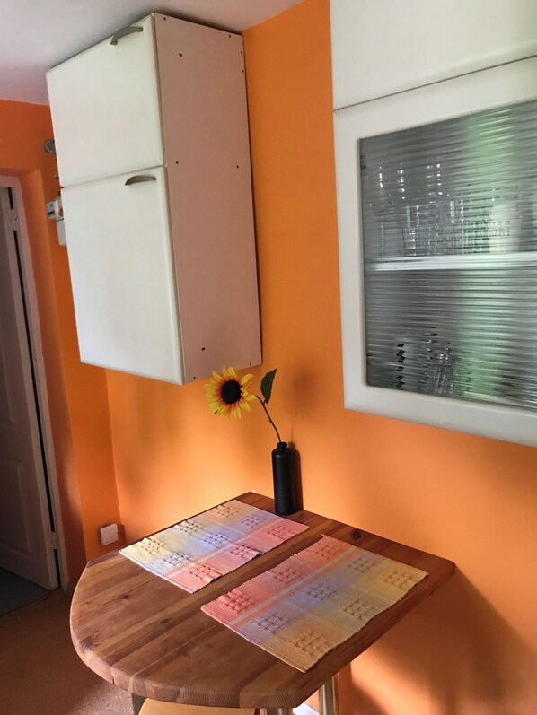 A room with a wooden table, a vase with a sunflower, and a window with blinds.