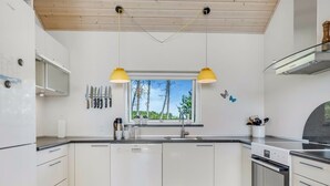 Moderni keittiö, jossa on valkoiset kaapit, sisäänrakennettu uuni ja ikkuna, josta avautuu näkymä puihin.