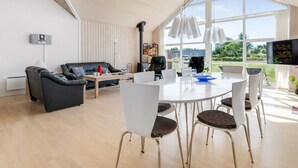 Moderni olohuone, jossa on ruokailutila, suuret ikkunat, takka ja litteänäyttöinen televisio.