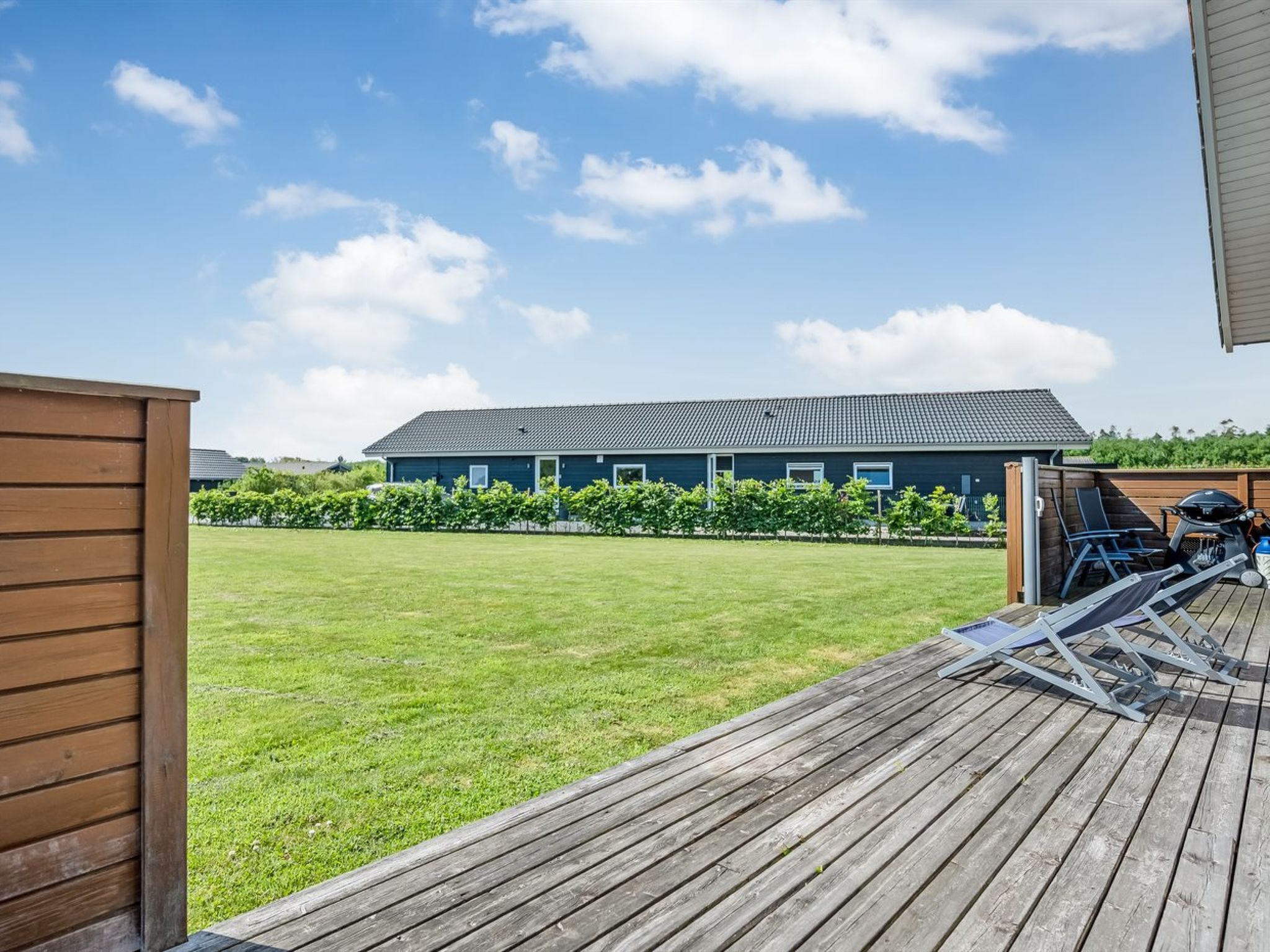 Een houten terras met uitzicht op een huis en een gazon.