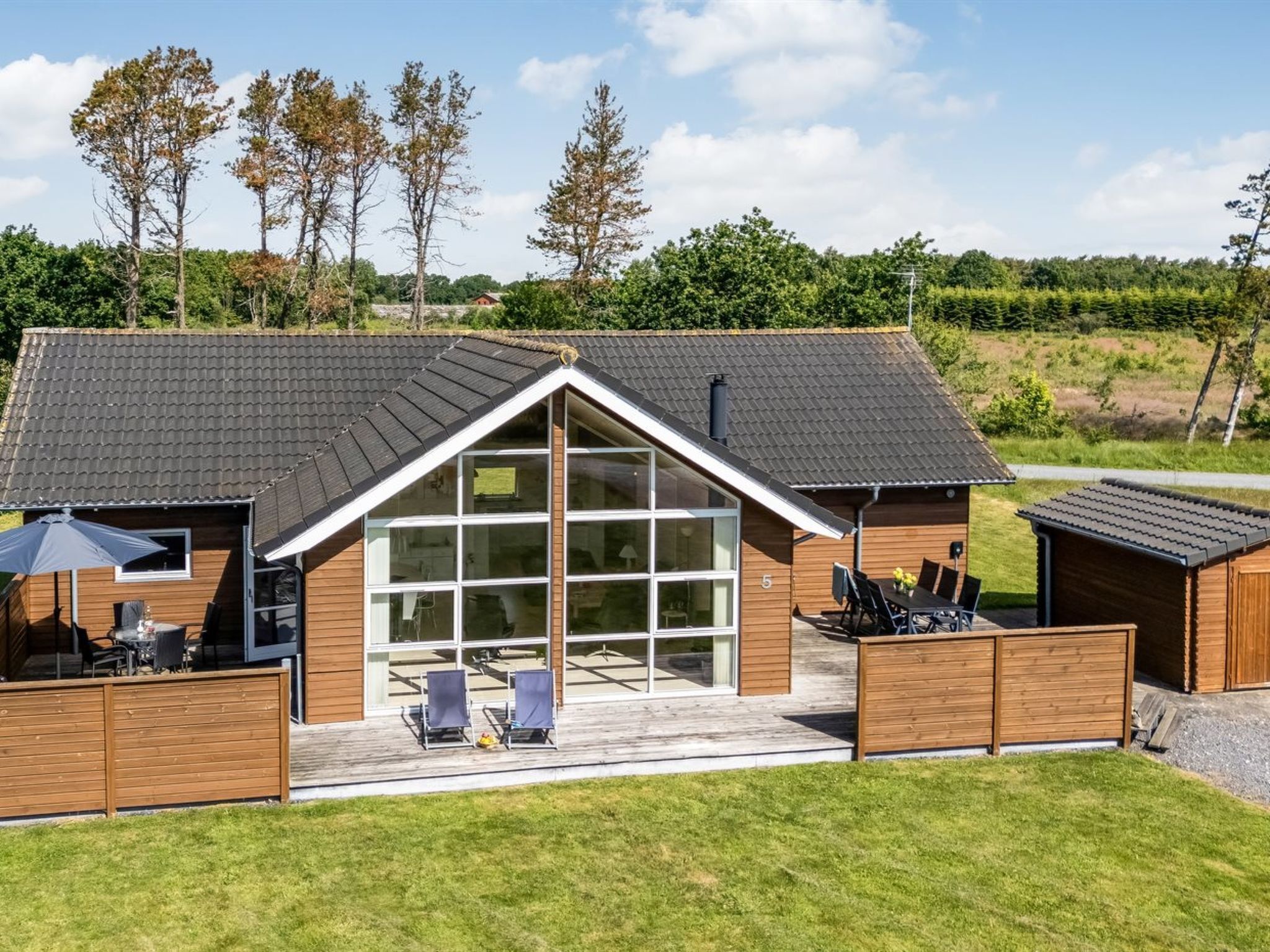 A modern house with a large garage, a covered patio with chairs, and a fenced yard.