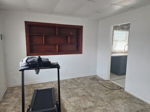 Habitación con estante de madera, cinta de correr y vista a una cocina a través de un vano.