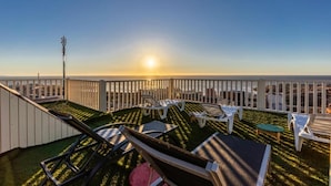 Een dak terras met ligbedden, een tafeltje en uitzicht op de ondergaande zon.