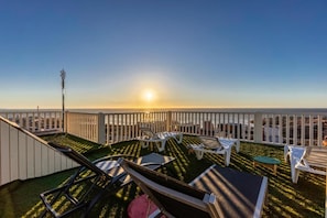 A rooftop terrace with sun loungers, a small table, and a view of the sunset.