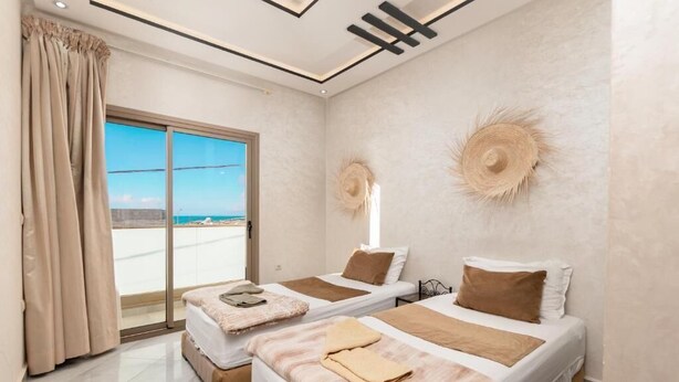 Een hotelkamer met twee bedden, een groot schuifglas en uitzicht op zee.