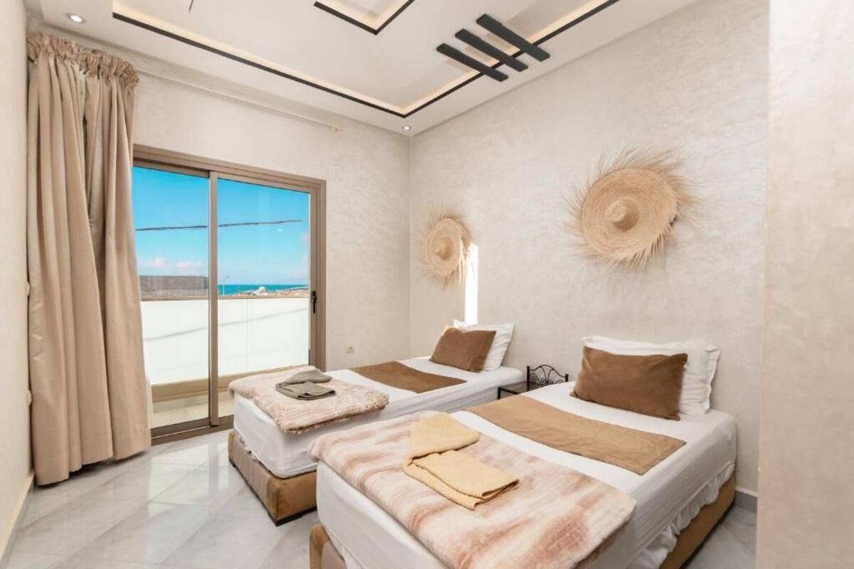 Habitació d'hotel amb dos llits, una gran porta corredissa de vidre cap a l'exterior i vista al mar.