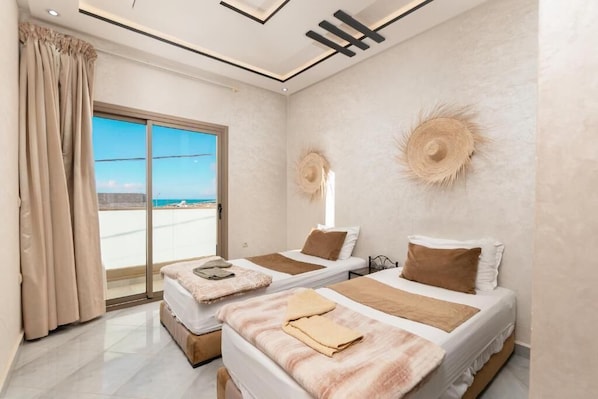 A hotel room with two beds, a large sliding glass door to the outside, and a view of the sea.