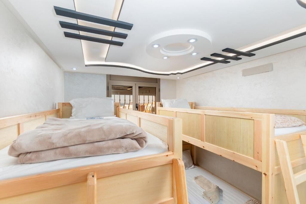 A room with bunk beds, a ceiling with recessed lighting, and a door leading to another room.