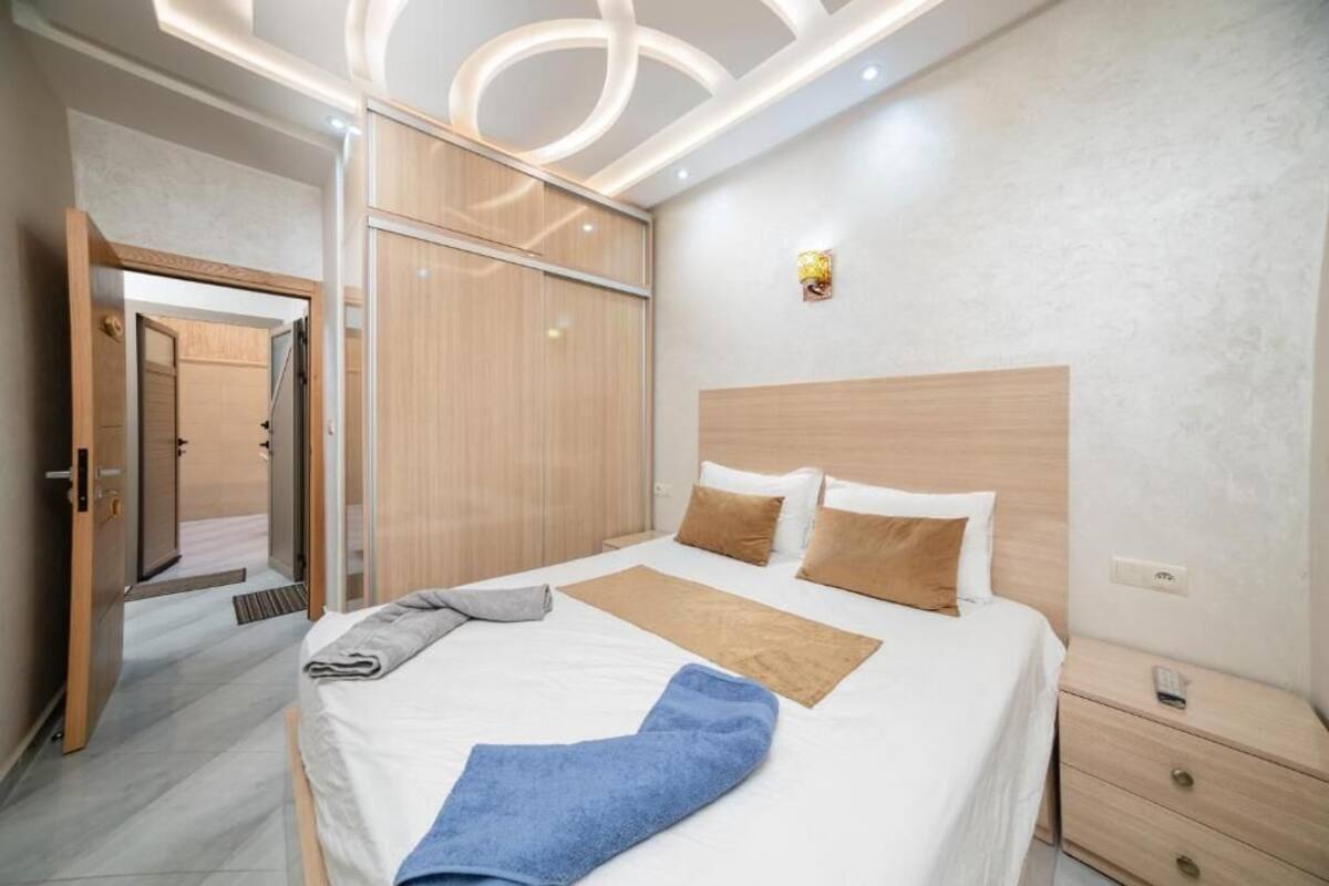 Habitació d'hotel moderna amb un llit gran, un armari de fusta, una taula de nit i una làmpada fixa a la paret.