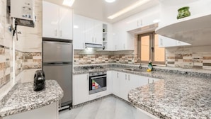 Een moderne keuken met witte kastjes, granieten werkbladen, een ingebouwde oven en een roestvrijstalen koelkast.