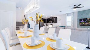 Ein moderner Essbereich mit einem weißen Tisch, gedeckt für vier Personen, gelben Tischsets, weißen Tellern und Tassen.