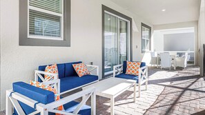 Eine Terrasse im Freien mit einer blauen Sofagarnitur, weißen Tischen und Stühlen.
