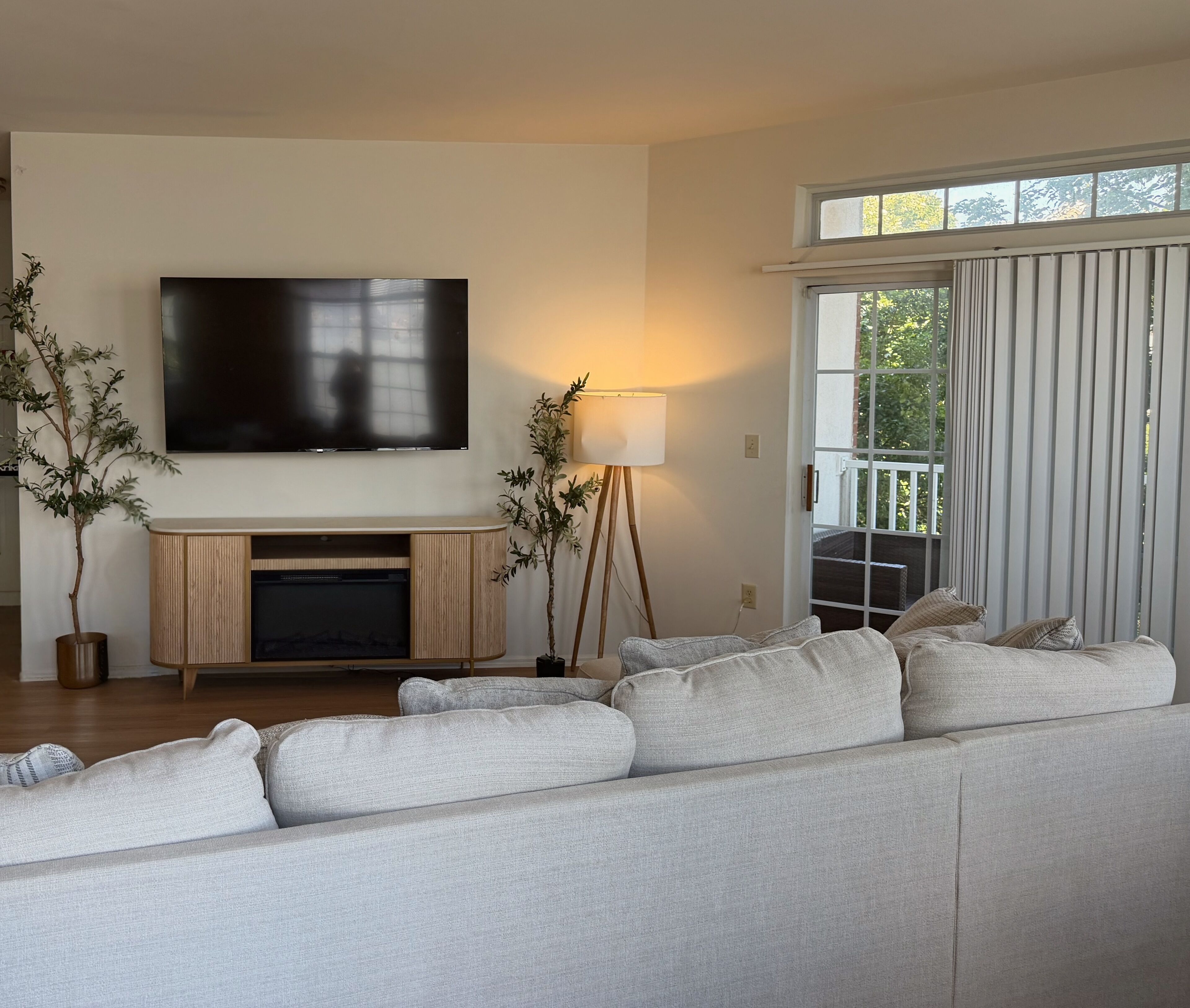 A living room with a flat-screen TV, a sofa, a lamp, and a view of the outdoors.