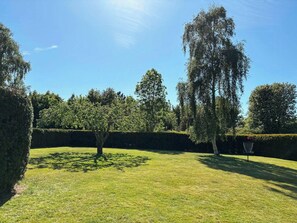 A well-maintained lawn with a variety of trees and a hedge.