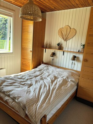 A wooden bed with a white striped bedspread, a woven pendant light, and a wall-mounted shelf with decorative items.