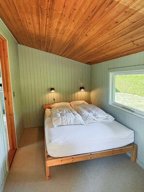 Ein Einzelbett mit Holzrahmen, zwei Nachttischlampen und ein Fenster mit Blick auf Grünflächen.