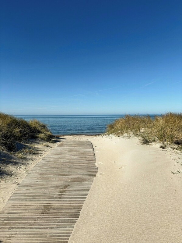 Ein Sandweg am Strand, der zum Meer führt, mit blauem Himmel.