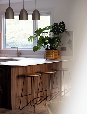 A kitchen with a wooden island, three stools, pendant lights, and a potted plant.