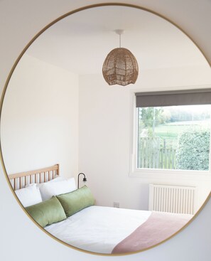 A bedroom with a bed, a window, a radiator, and a hanging light fixture. - Beautiful rural cottage in a tranquil East Lothian countryside setting (Haddington)