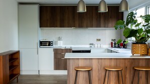 A modern kitchen with wooden cabinets, a central island with stools, pendant lighting, and a large plant.